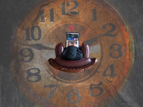 Person sitting on top of a clock dial with a MacBook on their lap