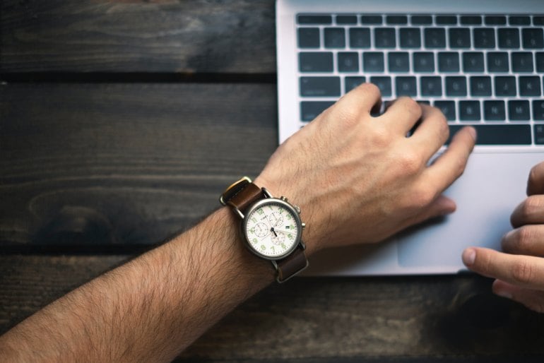 an arm with a wristwatch on top of an Apple MacBook