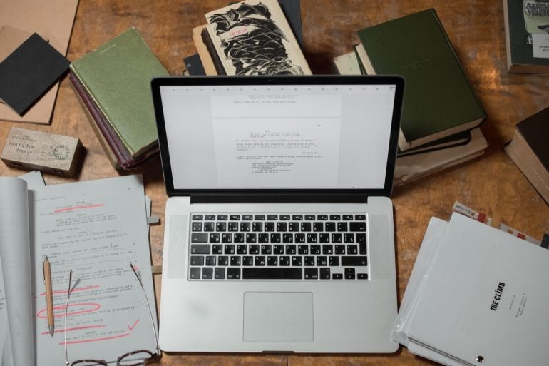 Laptop surrounded by documents and books on a desk